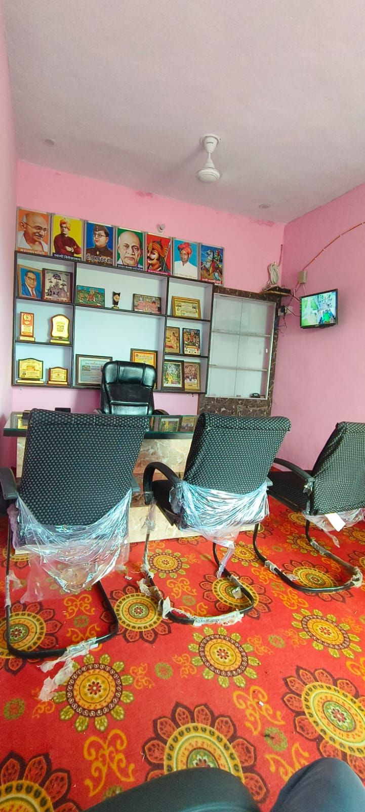 A foundation room with portraits of national figures on the wall, shelves of trophies and plaques, seating and a ceiling-mounted camera.