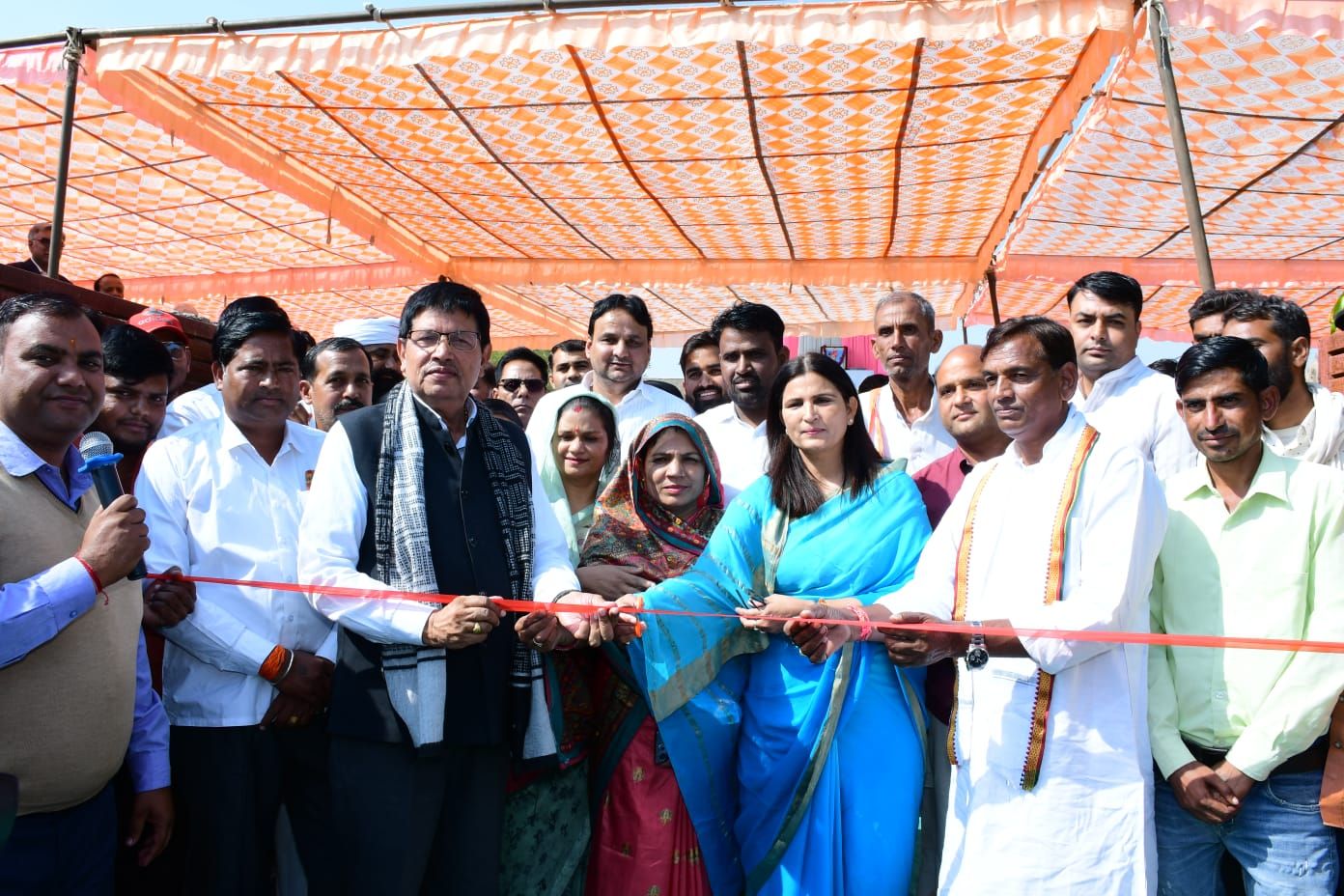 Guests and villagers standing together under an orange and white canopy, cutting a red ribbon at an inauguration.